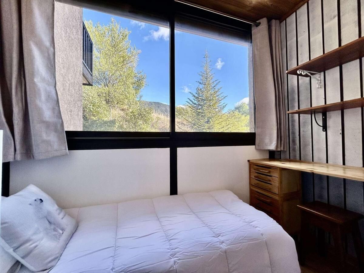 A bedroom with a bed, a wooden desk, and a window with a view of trees and hills.