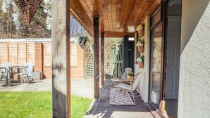 A covered patio area with wooden flooring, a seating arrangement, and a view of the backyard.