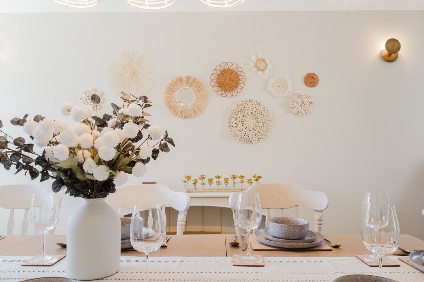 A dining area with a white table set for four, a vase of white flowers, and wall decor.