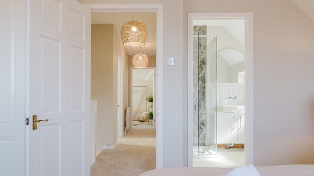 A bedroom with a bed, a bathroom with a glass shower, and a hallway leading to a dining area.