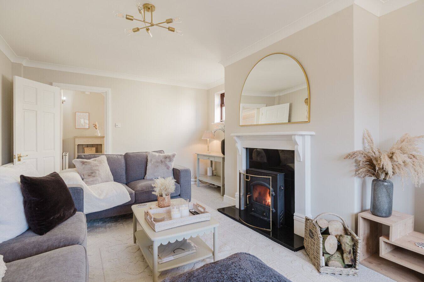 A cozy living room with a fireplace, a sofa, a coffee table, and a mirror.