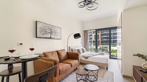 A modern hotel room with a brown leather sofa, a small dining table with two wine glasses, a bed with a view of the city, and a large window. - FIRST CLASS | Studio | Urban Elegance (Dubai)