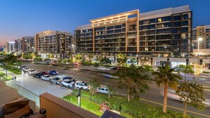 A modern multi-story hotel with a glass facade, a parking lot, and a well-lit street at dusk. - FIRST CLASS | Studio | Urban Elegance (Dubai)