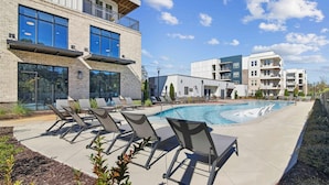 A modern building with a pool area, including lounge chairs and a clear blue sky. - Landing | Beautiful 2BD, Gym, Pool (Mableton)