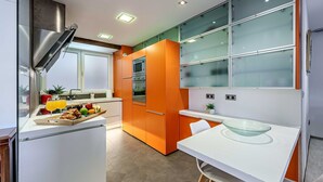 Une cuisine moderne avec des meubles de couleur orange, un plan de travail blanc et un saladier en verre posé sur une table blanche.