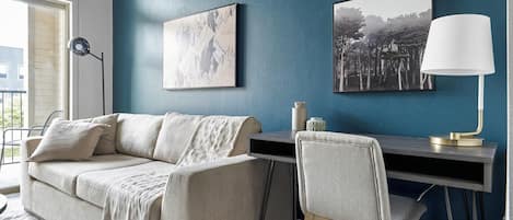 A living room with a sofa, a desk, and two framed pictures on the wall.