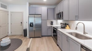 A modern kitchen with grey cabinets, stainless steel appliances, a microwave, and a sink. - Landing | Chic 1BD, Yoga Studio, Gym (Santa Rosa Beach)