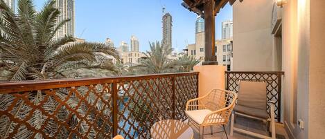 A balcony with wicker chairs, a wooden railing, and a view of tall buildings.