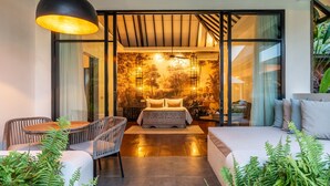 Een moderne slaapkamer met een groot bed, een zithoek met een tafel en stoelen, en uitzicht op een boswanddecoratie.