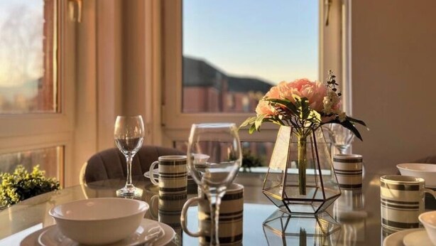 Une table à manger ornée d’un vase de fleurs, de tasses à rayures et d’un verre à vin.