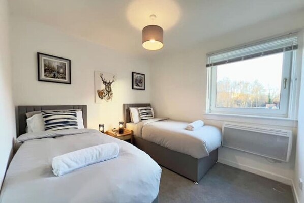 A bedroom with two beds, a ceiling light, framed pictures, and a window with blinds.