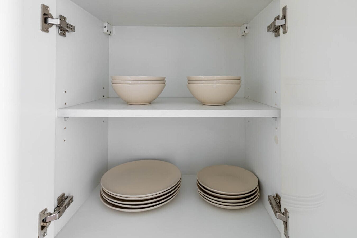 Un meuble blanc à deux étagères, chacune contenant un bol et une pile d’assiettes.