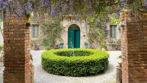 Un patio con una puerta verde, paredes de ladrillo y un seto circular.