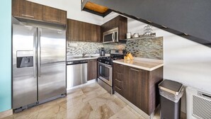 A modern kitchen with stainless steel appliances, dark wood cabinets, a tiled backsplash, and a small island with a sink.