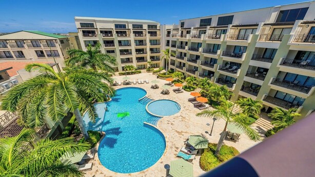 A hotel with multiple swimming pools surrounded by palm trees and lounge chairs.