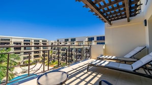 A balcony with sun loungers, a pool, and a view of a multi-story building.