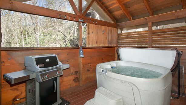 Eine Holzhütte mit Whirlpool, Grill und Fenster mit Blick auf Bäume.