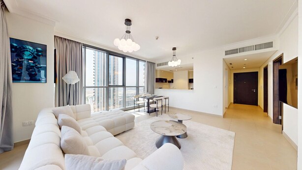Een moderne woonkamer met een grote bank, een eethoek en een keuken op de achtergrond.