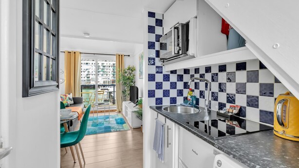 A modern kitchen with a microwave, sink, and kettle. It features a checkered backsplash and a view of the city through large windows. - On the Water 6 with Free Parking | By My Getaways (Brighton)
