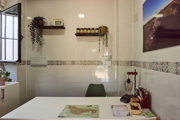 Una habitación con un mapa, un escritorio, una silla, una estantería con botellas, una planta colgante y un aplique de pared.