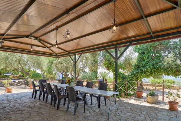 Un patio exterior con zona de estar cubierta, suelo de piedra y plantas en macetas.