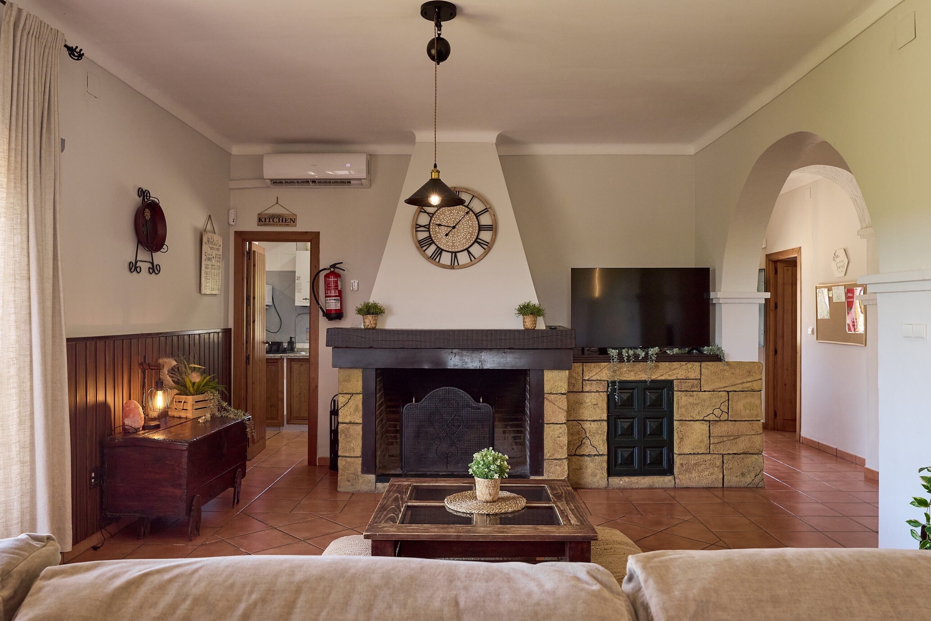 Una sala de estar con chimenea, un reloj y un televisor.