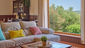 Una sala de estar con un sofá, un aparador de madera y un ventanal con vistas a zonas verdes.