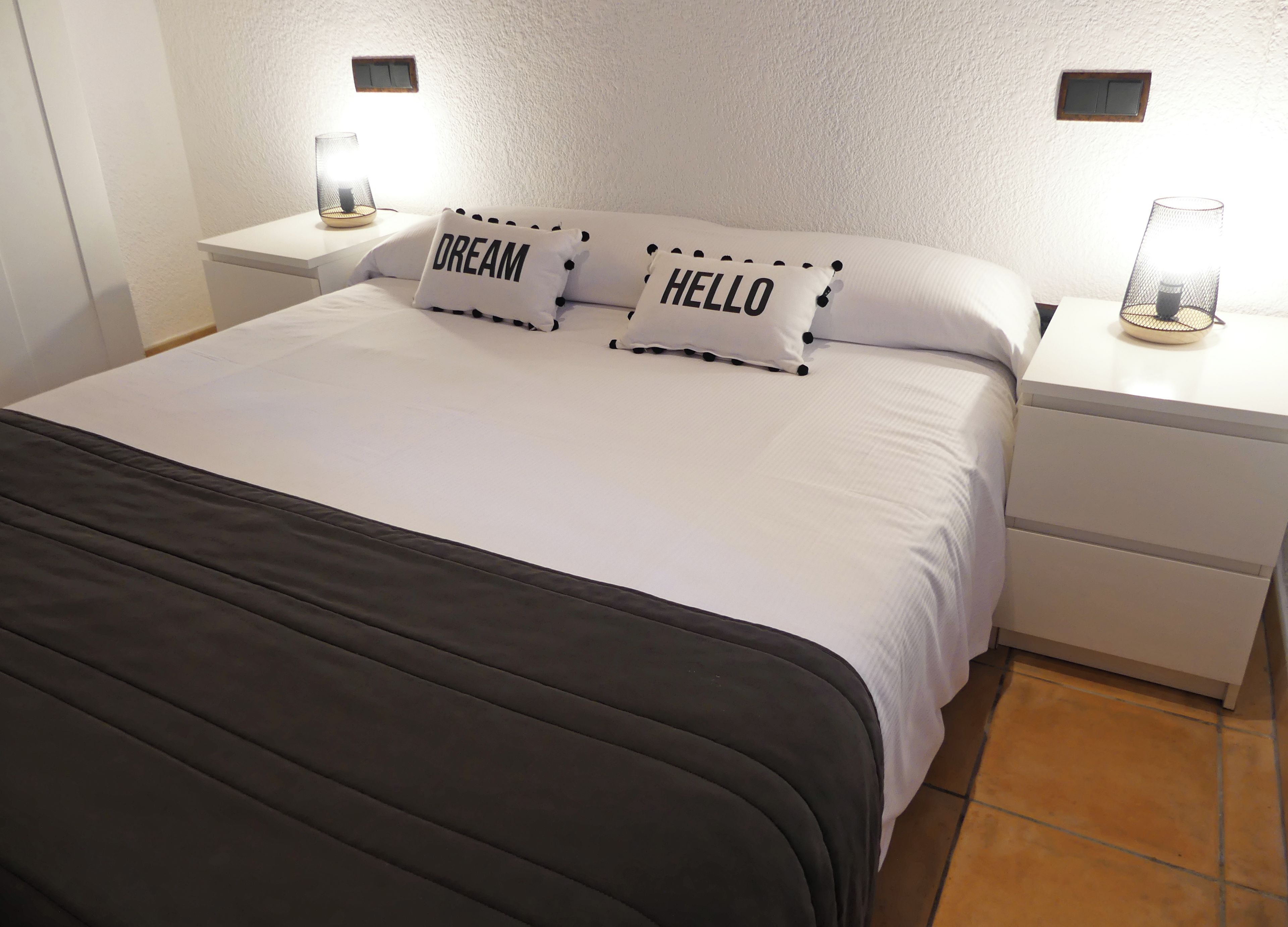 A neatly made bed with two pillows, one with 'DREAM' and the other with 'HELLO' on them.
