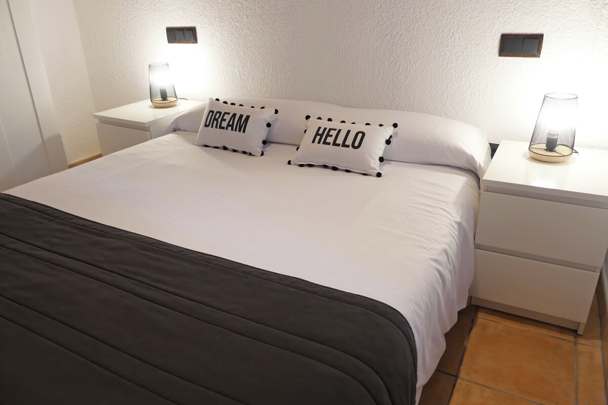 Ein ordentlich bezogenes Bett mit zwei Kissen, eines mit dem Aufdruck 'DREAM' und das andere mit 'HELLO'.