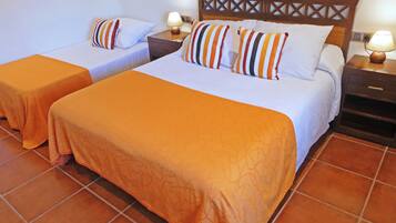 Una habitación de hotel con dos camas, cada una con colcha naranja y almohadas a rayas. Hay mesitas de noche de madera con lámparas y un cabecero de madera con diseño de celosía.