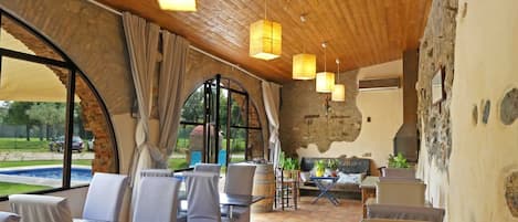 A rustic dining area with wooden ceiling, large windows, and a view of the outdoors.