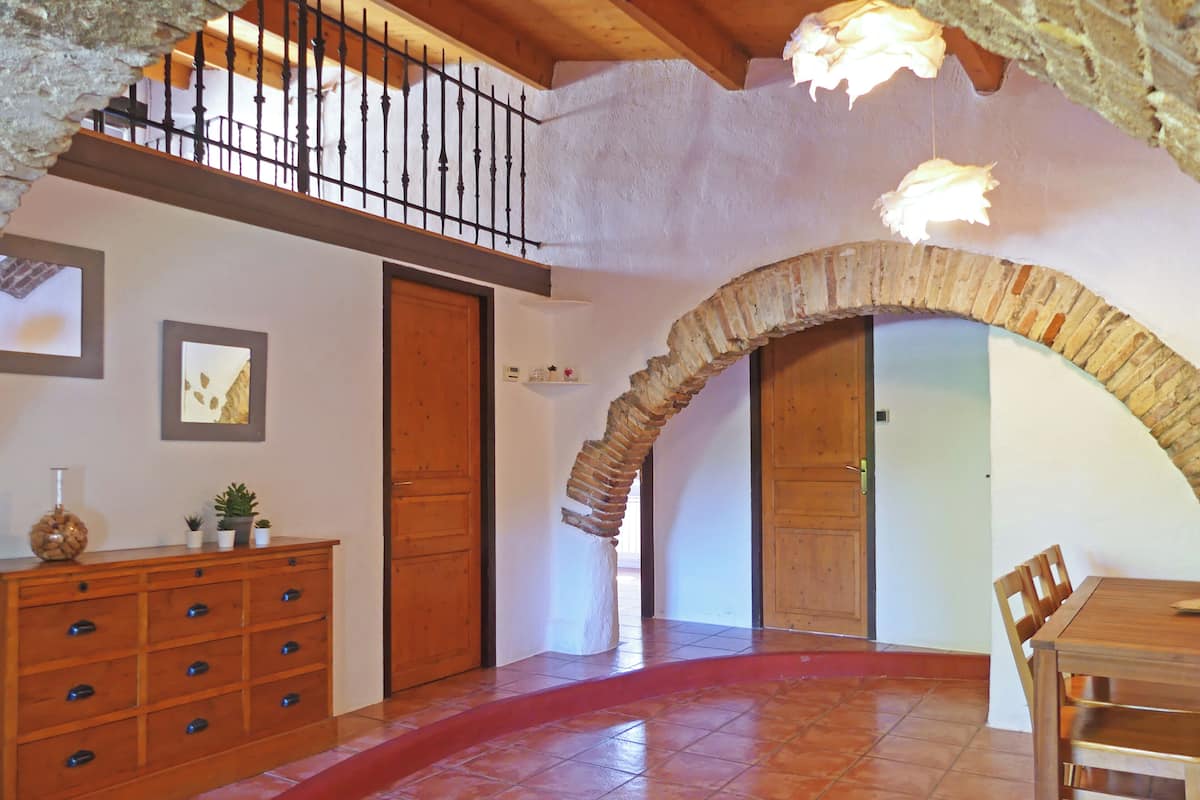 Une pièce spacieuse avec un escalier en bois, un sol carrelé de tuiles rouges et une table à manger en bois, accompagnée de chaises.