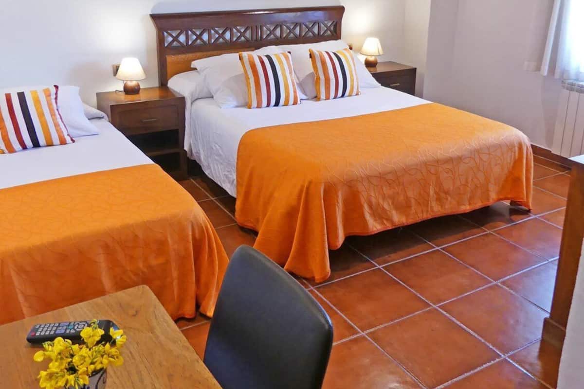 A hotel room with two beds, a wooden headboard, a table with a vase of flowers, and a chair.