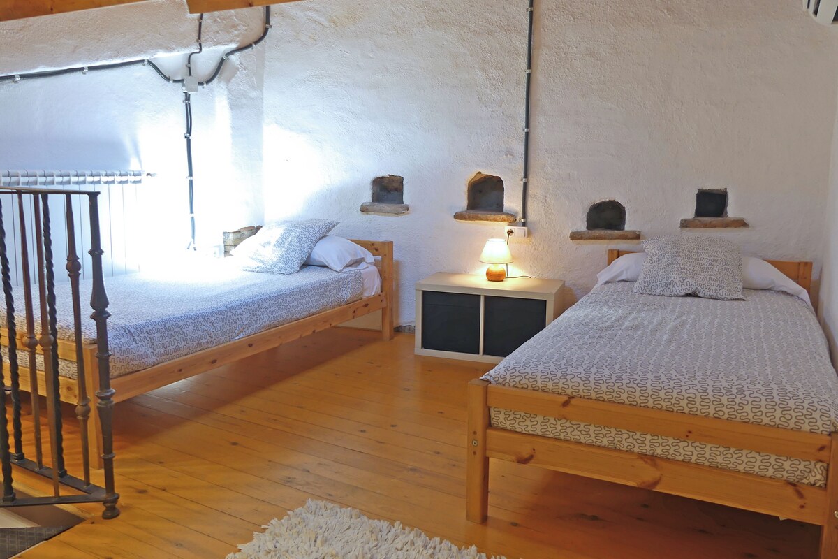 Een knus slaapkamer met twee houten bedden, een nachtkastje met een lamp en een landelijke wanddecoratie.
