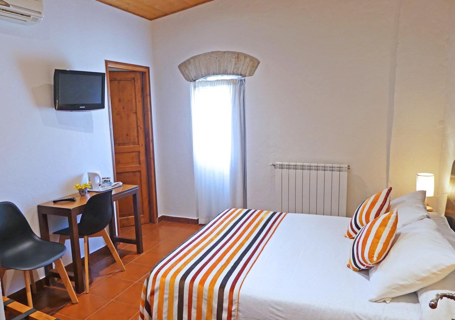 Une chambre d’hôtel équipée d’un lit, d’un bureau, d’une chaise, d’une télévision et d’une fenêtre avec des rideaux.