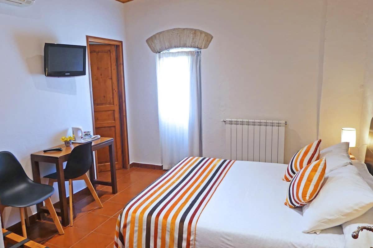 Une chambre d’hôtel équipée d’un lit, d’un bureau, d’une chaise, d’une télévision et d’une fenêtre avec des rideaux.