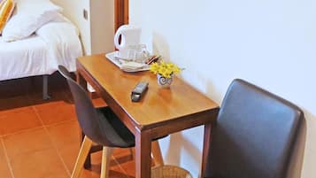Une petite pièce avec un lit, une table en bois sur laquelle se trouve une télécommande, une tasse blanche et un vase avec des fleurs jaunes.