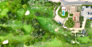 Luchtbeeld van een golfbaan met zandbunkers, een zwembad en een gebouw met pannendak.