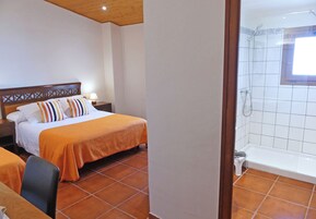 Habitación de hotel con cama, mesita de noche, silla, baño con bañera y ventana.