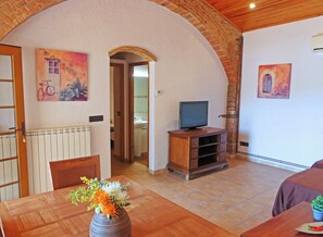 Een kamer met een eettafel, stoelen, een tv op een houten dressoir en een vaas met bloemen.