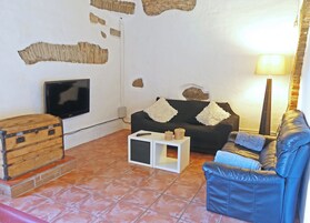 Una sala de estar con televisión, un sofá, un sillón de cuero, una lámpara y una pequeña mesa con un control remoto.