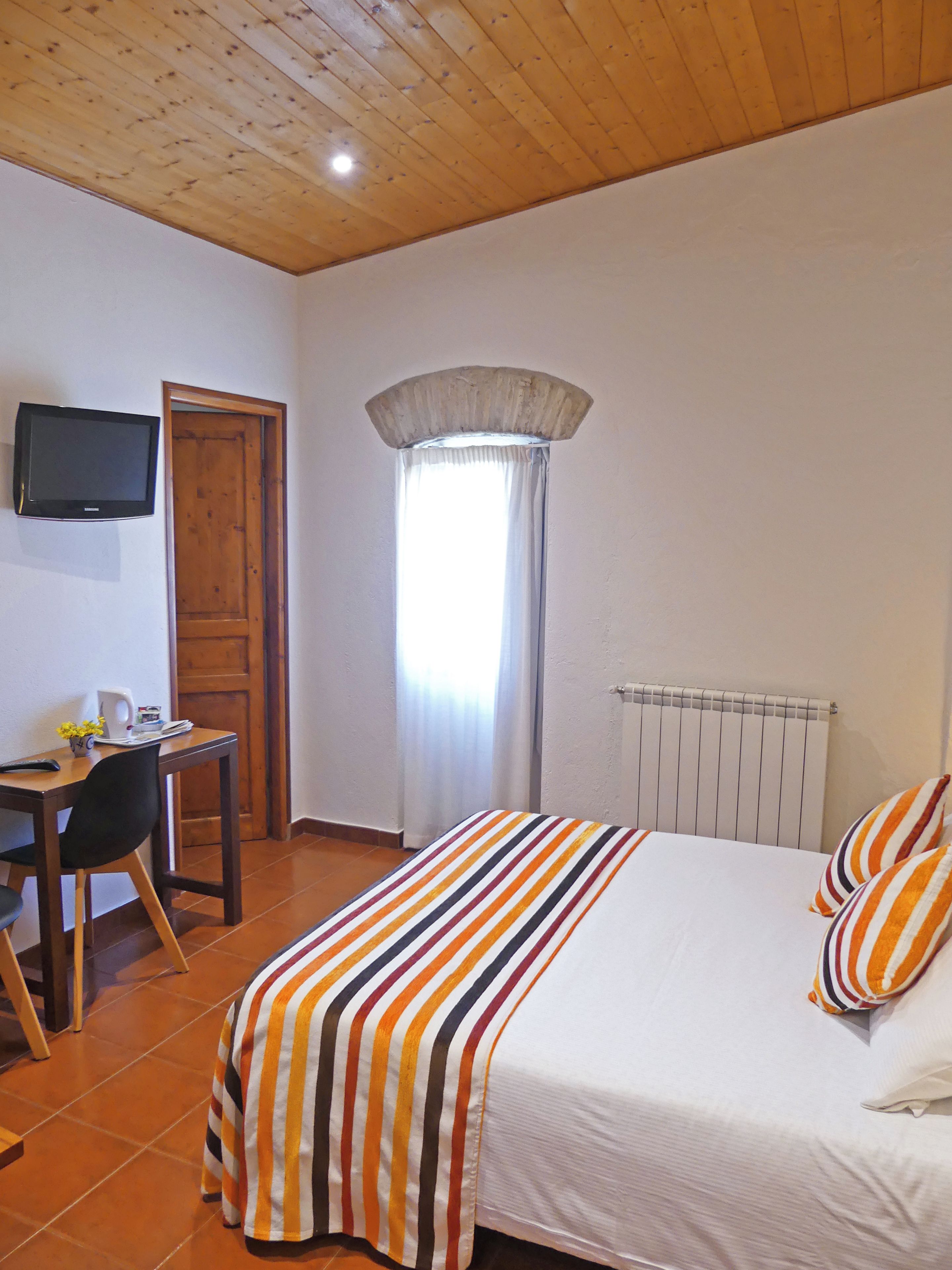 Une chambre à coucher avec un lit, un bureau, une chaise, un téléviseur et une fenêtre avec des rideaux.