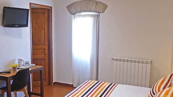 Une chambre à coucher avec un lit, un bureau, une chaise, un téléviseur et une fenêtre avec des rideaux.