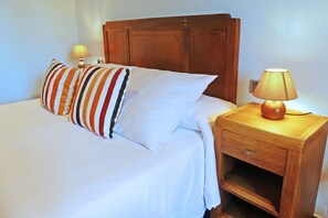 Un lit bien fait, avec des oreillers à rayures, une tête de lit en bois et une table de chevet surmontée d’une lampe.