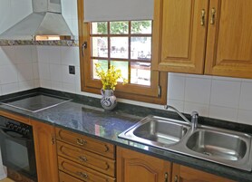 Una cocina con armarios de madera, un lavamanos de acero inoxidable, una estufa y una ventana con vistas al exterior.