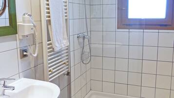 Un baño con lavamanos blanco, un taburete pequeño, ducha con puerta de cristal y una ventana.