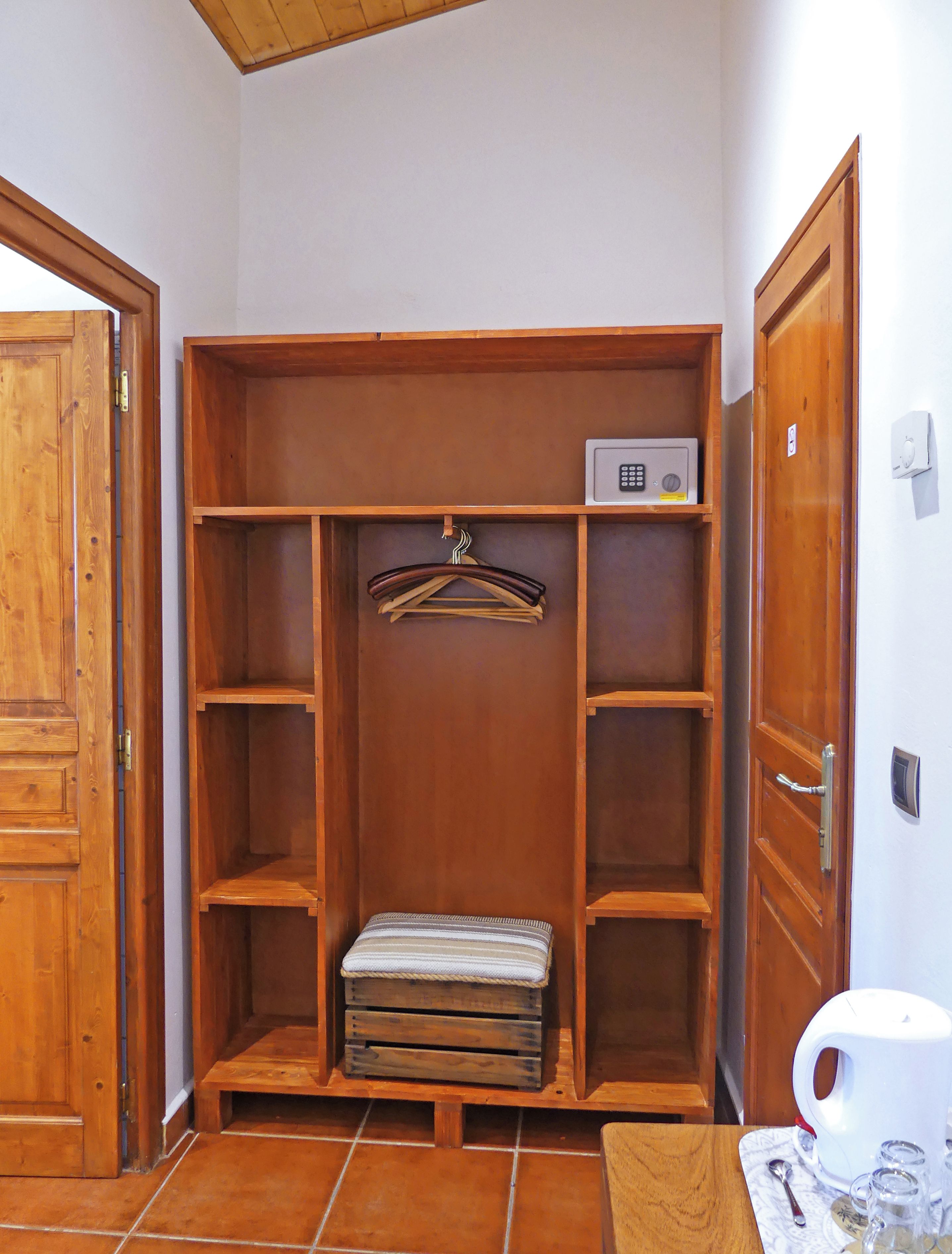 A wooden wardrobe with multiple shelves and a hanging rod, a small bench, and a microwave on the top shelf.
