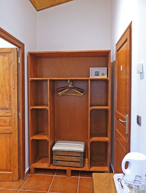 Une armoire en bois avec plusieurs étagères et une tringle pour suspendre les vêtements, un petit banc et un four à micro-ondes placé sur l’étagère supérieure.
