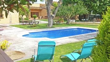 Una piscina con dos sillones turquesa, rodeada de un césped cuidado y varios árboles.