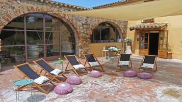 Une terrasse avec des chaises longues et une petite table, entourée d’arches en pierre et d’un bâtiment jaune.